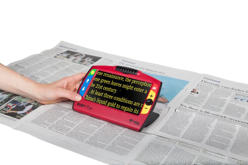 A person's hand holding a Ruby 7 HD over a newspaper article